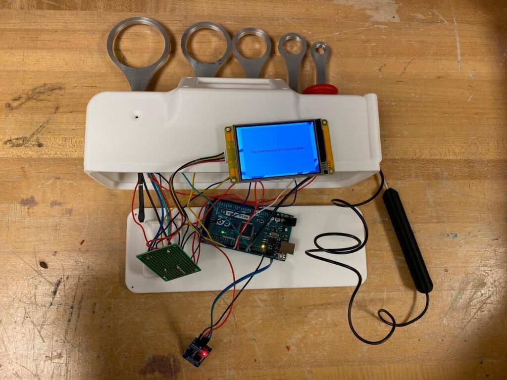 A custom-built embedded system featuring an Arduino board, wiring, sensors, a Nextion display, and conductive metal rings used for an engineering technology project.